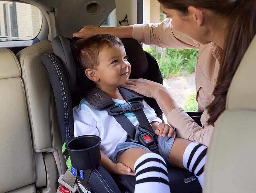 A woman checking the harness height for a child in a forward-facing car seat.