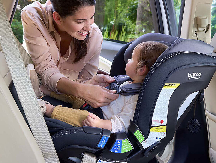 A woman adjusting the chest clip for a child in a rear-facing car seat.