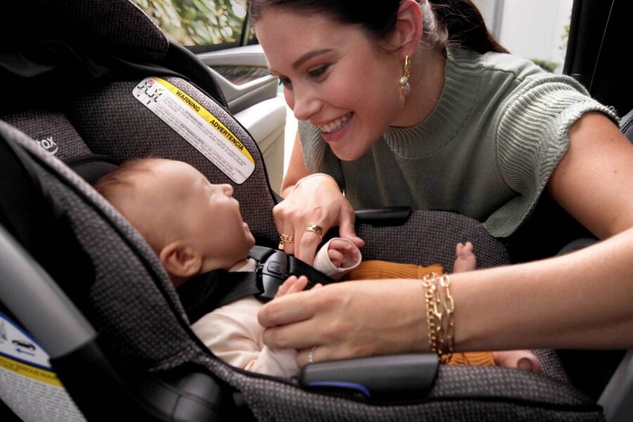 Someone leans into a car to engage with a smiling baby secured rear-facing in an infant car seat.