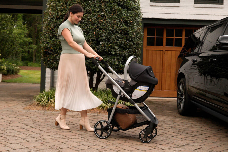 Woman pushing a travel system towards a parked car in a driveway