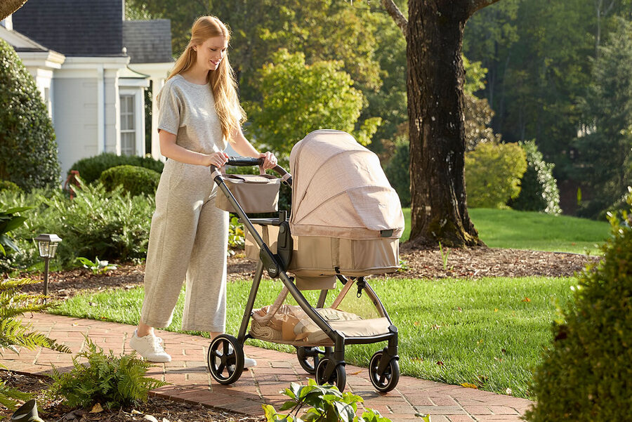 A woman pushing a baby stroller along a path outside on a sunny day.