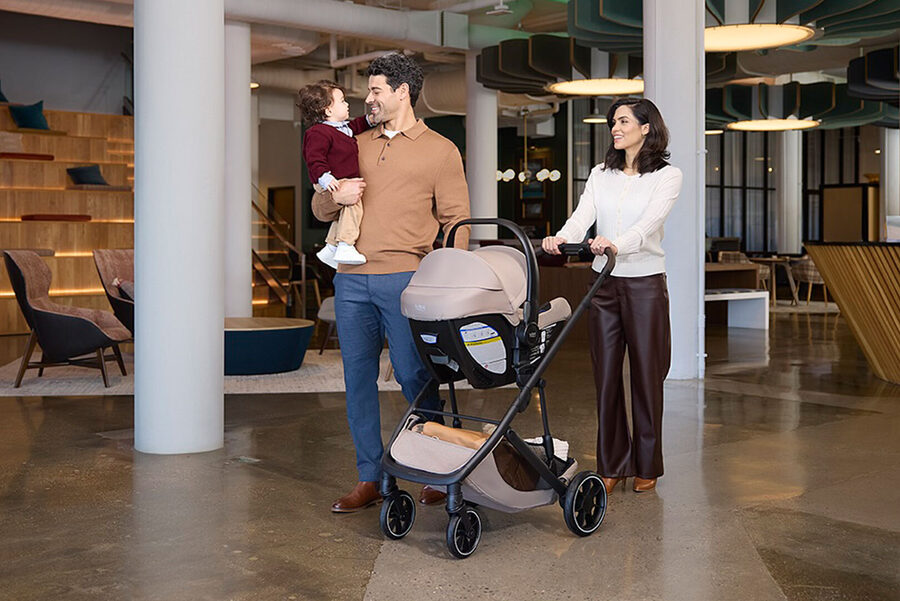 A man and a woman walking inside. The man is carrying a young toddler, and the woman is pushing a stroller.