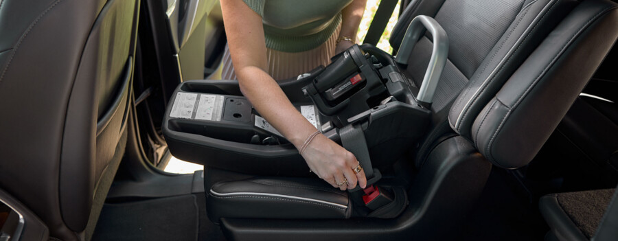 A woman installing a car seat base in a vehicle using the seat belt.
