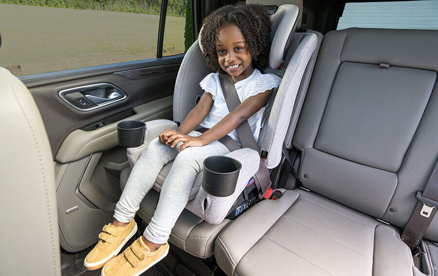 A smiling child in a high-back booster seat in the back seat of a car.