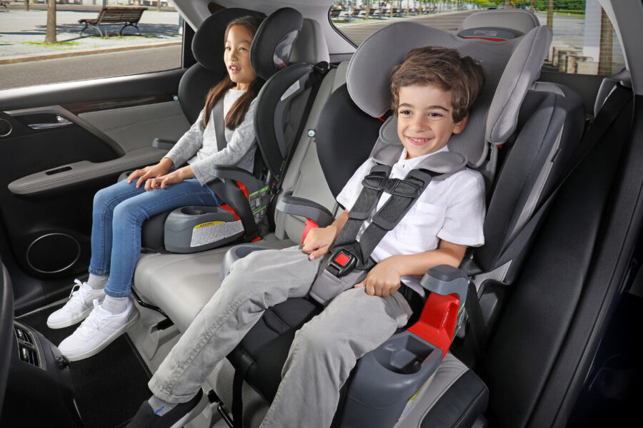 Two children in car seats. One is in a booster, the other is in a forward-facing car seat with a harness.