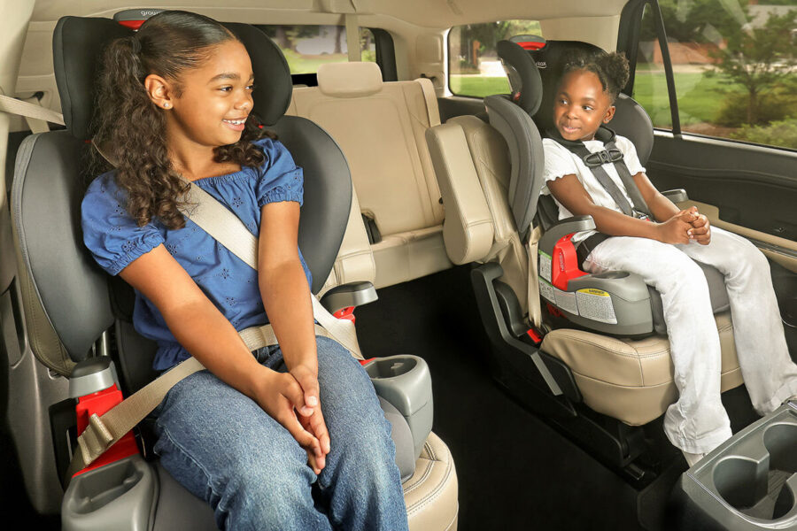 Two children in car seats. One is in a booster, the other is in a forward-facing car seat with a harness.