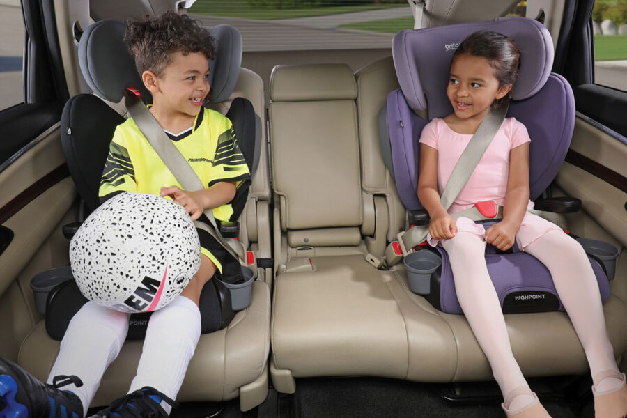 Two children in the back seat of a vehicle in booster seats. One is wearing athletic gear, the other is in a ballet outfit.