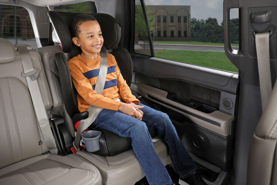 child in a high-back booster seat in the back of a vehicle.