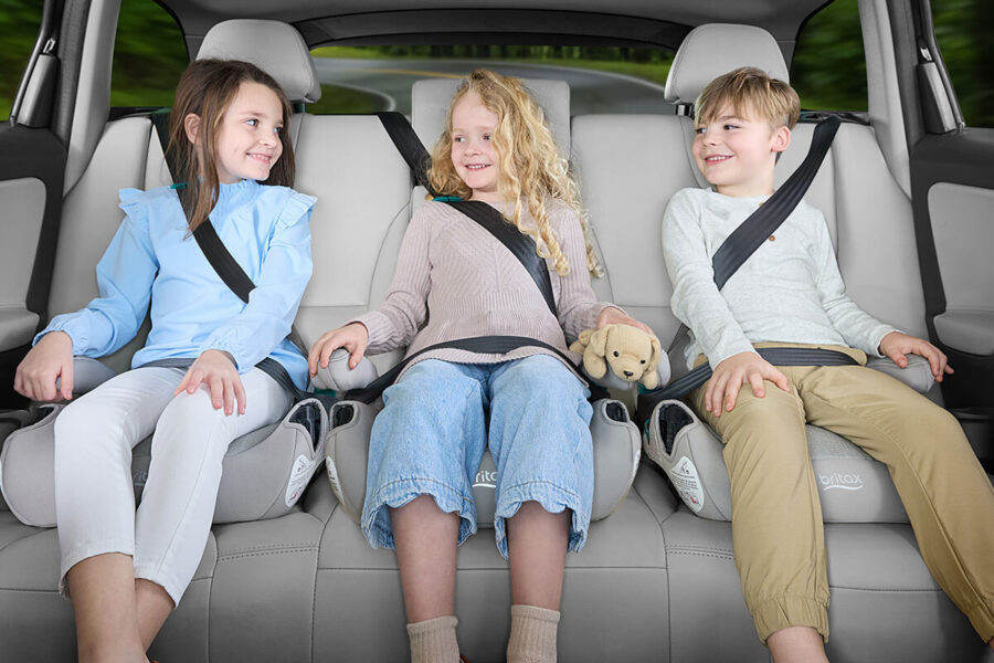 Three children in backless booster car seats in the back seat of a vehicle. 