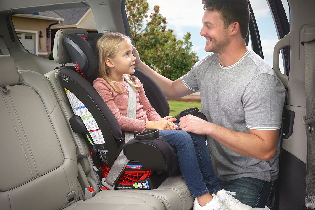 A child sitting in a high-back booster seat in the back seat of a vehicle.