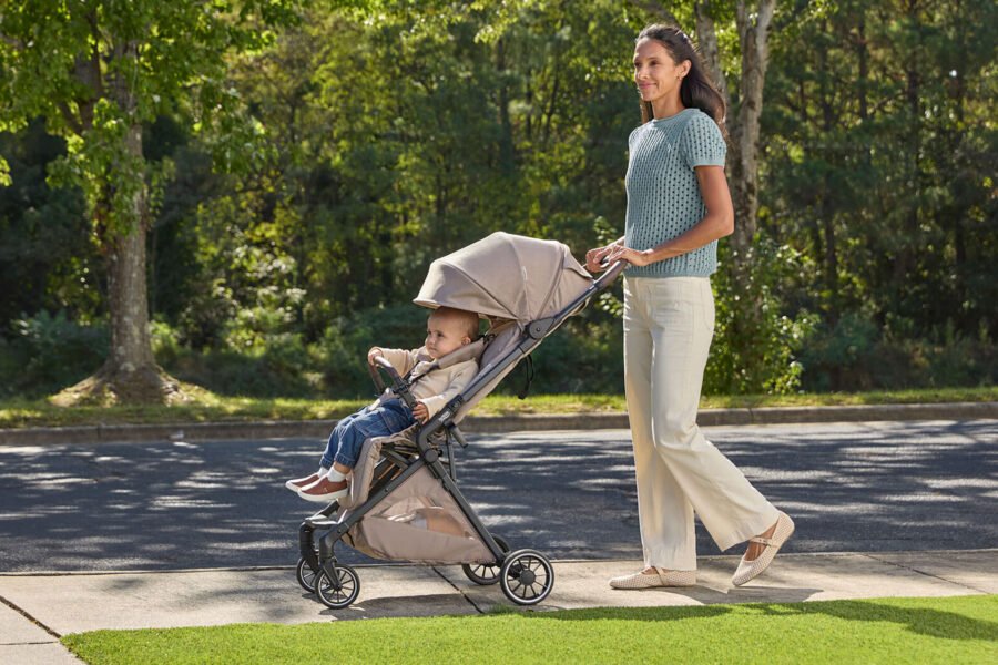 A woman pushing a toddler in a stroller along a sidewalk on a bright, sunny day.