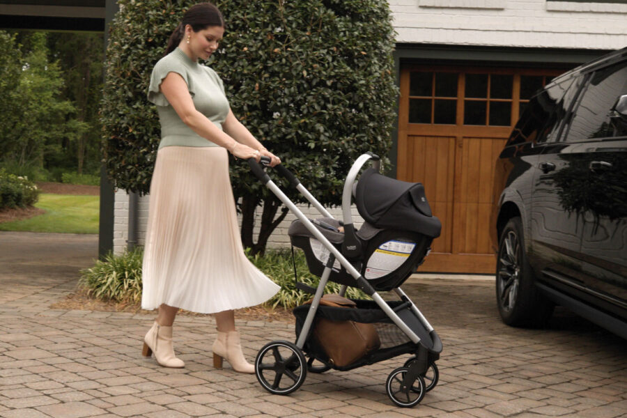 A woman outside pushing a travel system stroller while approaching a parked vehicle.