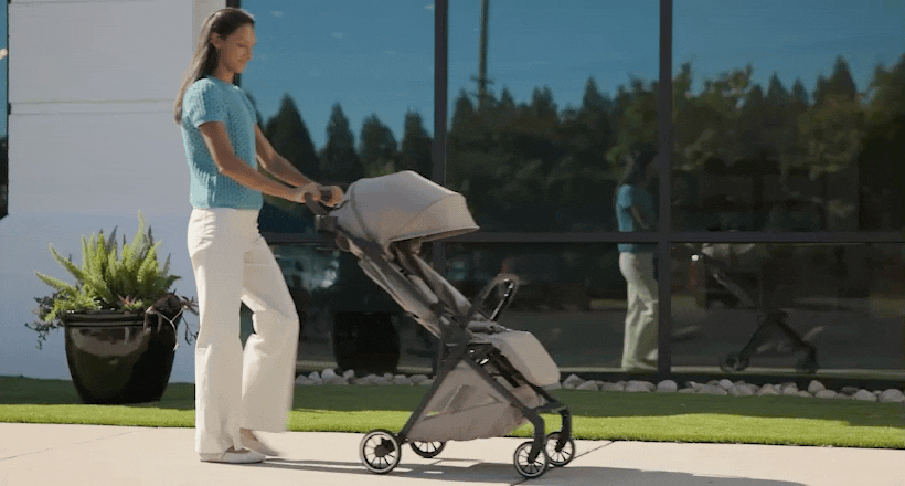 A woman folds a stroller, picks the stroller up by the handle, and walks away.