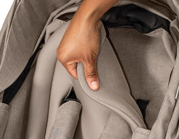 Someone lifting up the seat insert on a stroller, revealing mesh fabric on the back.