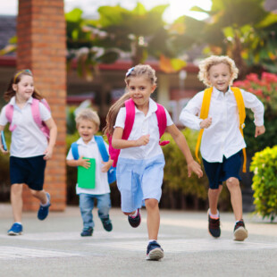 Four children wearing backpacks and walking together outdoors.