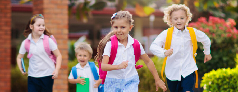 Four children wearing backpacks and walking together outdoors.