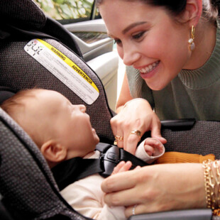 A baby in a car seat looking up at a woman.