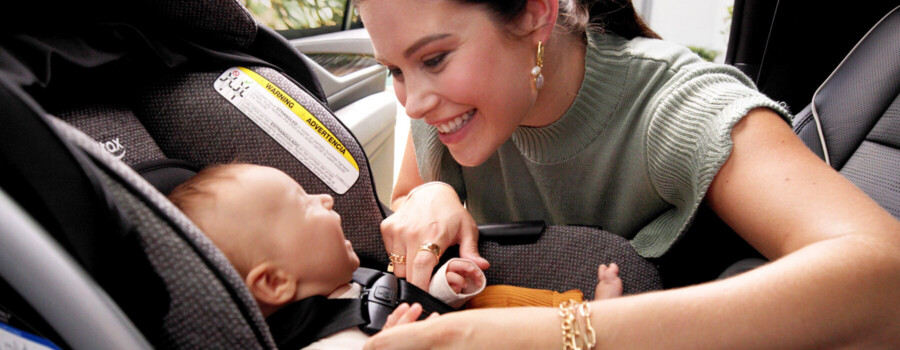 A baby in a car seat looking up at a woman.
