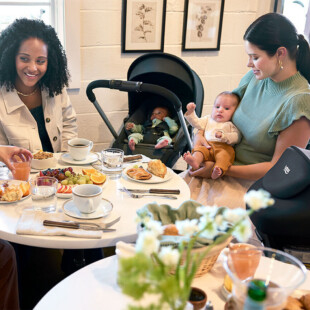 Three women and two babies around a table with food and beverages.