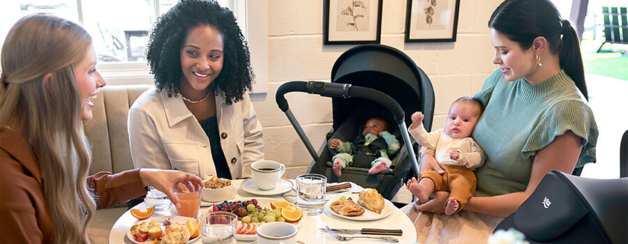 Three women and two babies around a table with food and beverages.