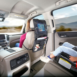 A child in a car seat in the back of a vehicle looking at a tablet. The tablet is inside of a vehicle seatback organizer.