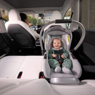 A smiling baby buckled into a rear-facing car seat in the back seat of a vehicle.