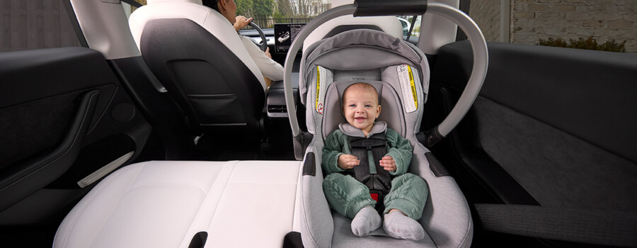 A smiling baby buckled into a rear-facing car seat in the back seat of a vehicle.