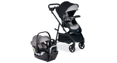 Ride side view of a grey and black infant car seat in a base next to a grey and black baby stroller.
