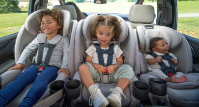 A child, a toddler, and a baby in slim rear-facing car seats, lined up 3 across in the back of a vehicle.