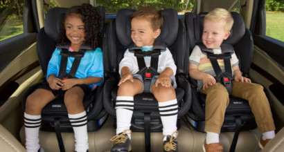 Three children sitting in forward-facing car seats in the back seat of a car. 
