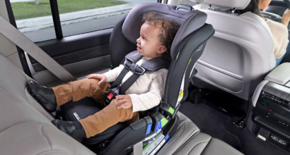 A toddler sitting in a rear-facing car seat in the back of a car, looking out the window with a pleasant look on his face.