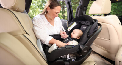 Mother interacting with baby in a rear-facing infant car seat in the back of a vehicle.