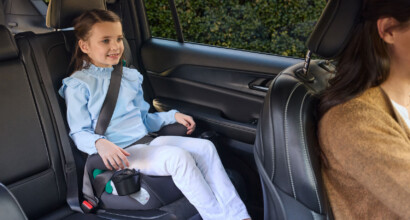 A child sitting up straight with good posture in a booster seat in the back of a car.