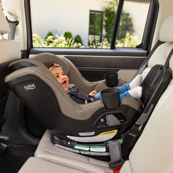 A smiling baby in a rear-facing rotating convertible car seat, which is installed in the back seat of a vehicle.