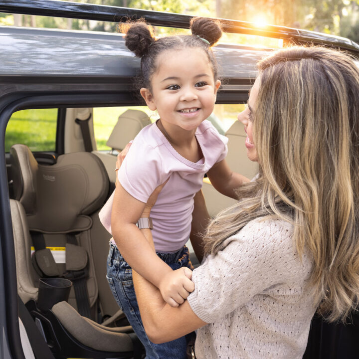 A woman lifting a child out of a car seat, holding the child up and smiling at her.