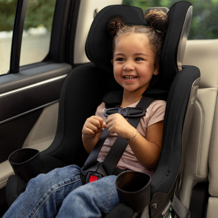 A happy, smiling child buckled into a forward-facing car seat in a vehicle.