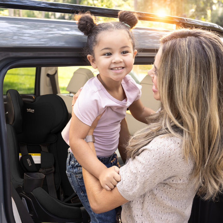 A woman lifting a child out of a car seat, holding the child up and smiling at her.