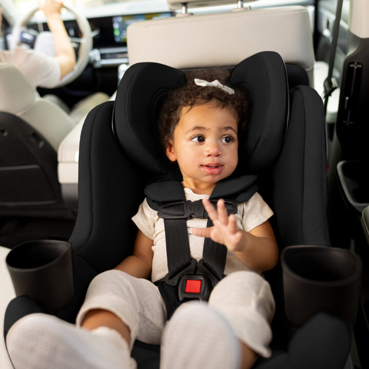 A toddler buckled up in a black rear-facing car seat with a 5-point harness.