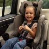 A happy, smiling child buckled into a forward-facing car seat in a vehicle.