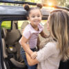 A woman lifting a child out of a car seat, holding the child up and smiling at her.