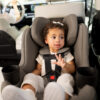 A toddler buckled up in a black rear-facing car seat with a 5-point harness.