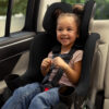 A happy, smiling child buckled into a forward-facing car seat in a vehicle.