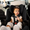A toddler buckled up in a black rear-facing car seat with a 5-point harness.